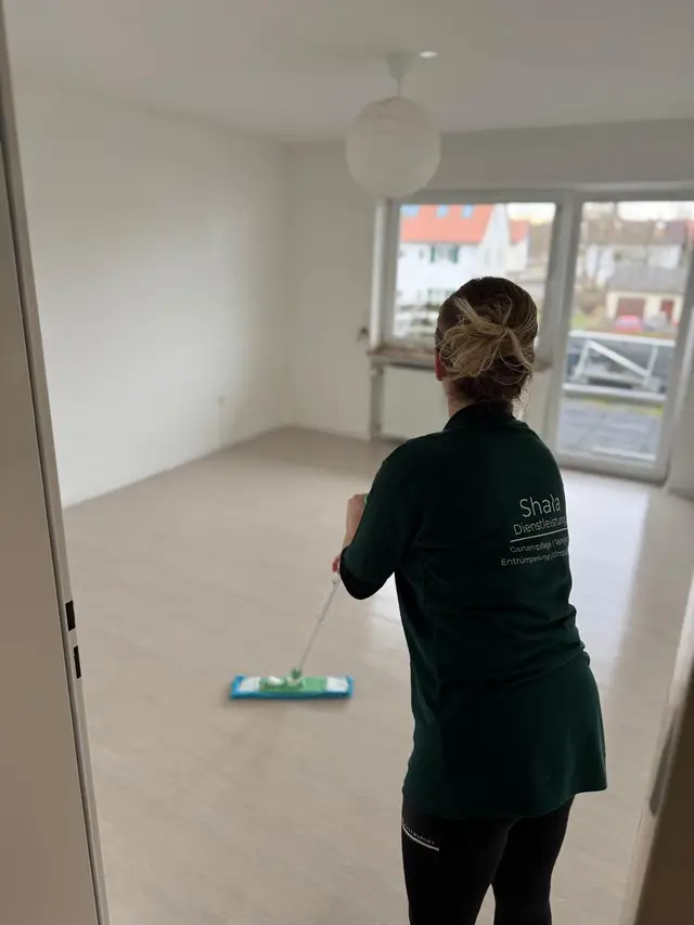 Mitarbeiterin wischt den Boden einer leergeräumten Wohnung