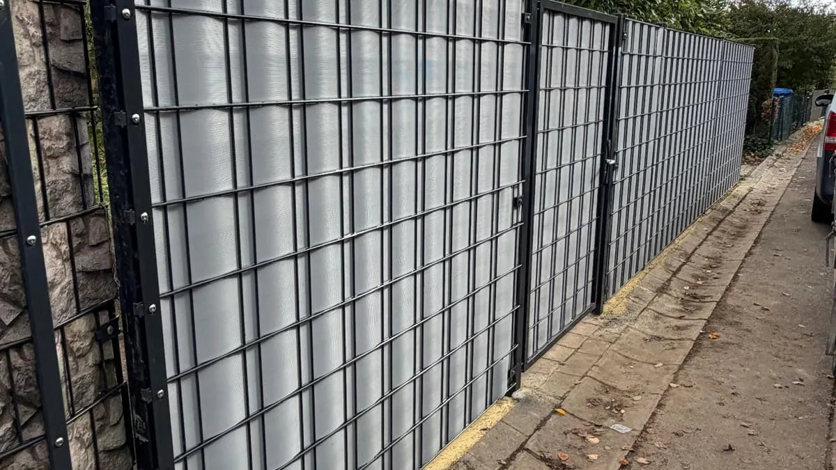 Doppelstabmattenzaun mit grauen Sichtschutzstreifen entlang eines Gehwegs